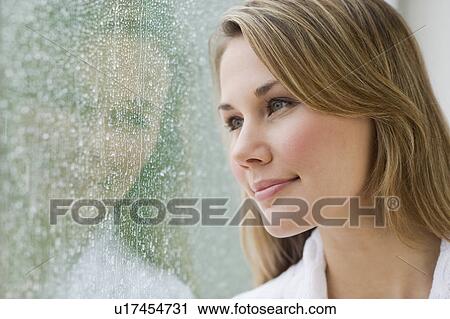 Stock Image - Woman looking out rainy window. Fotosearch