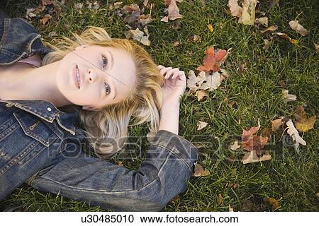 Woman lying in grass on a fall day View Large Photo Image Stock Image - Woman lying in grass on a fall day. Fotosearch