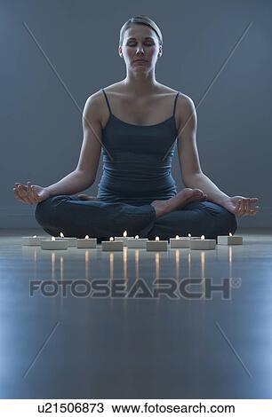 Stock Image - Woman meditating next to candles. Fotosearch
