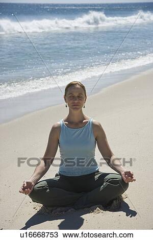 Stock Image - Woman practicing yoga at beach. Fotosearch