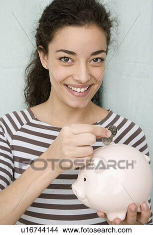 Picture - Woman putting coins in piggy bank. Fotosearch