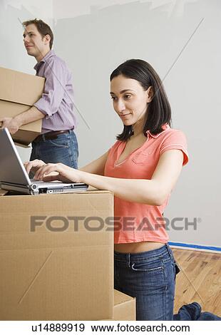 Woman using laptop while man carries box in new house View Large Photo Image Stock Photo - Woman using laptop while man carries box in new house. Fotosearch