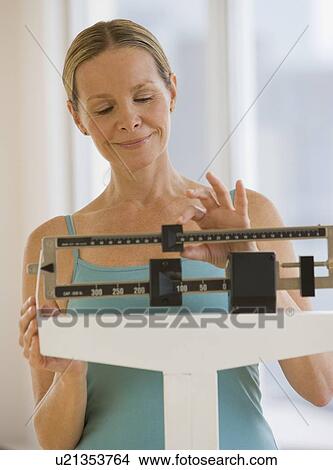 Picture - Woman weighing self on scale. Fotosearch