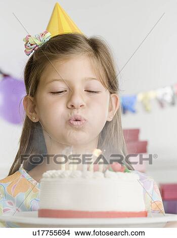 Picture - Young girl blowing out candles on cake. Fotosearch