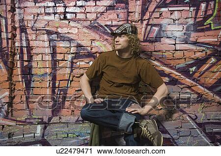 Young man sitting in front of graffitied wall View Large Photo Image Stock Image - Young man sitting in front of graffitied wall. Fotosearch