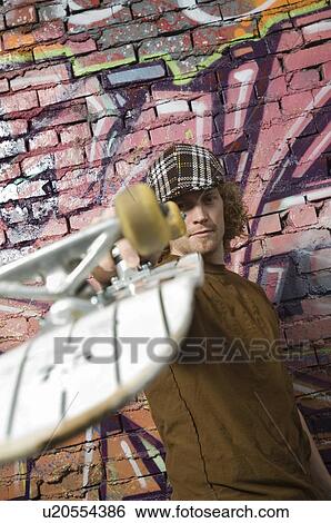 Stock Photograph - Young man with skateboard in front of graffitied wall. Fotosearch
