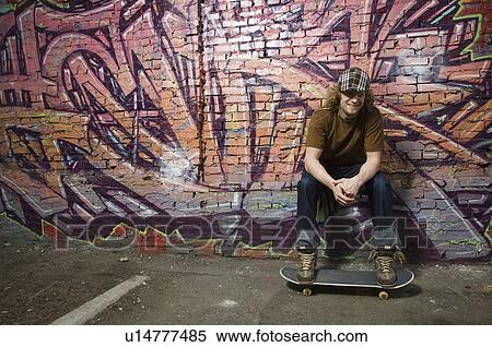 Stock Photography - Young man with skateboard in front of graffitied wall. Fotosearch