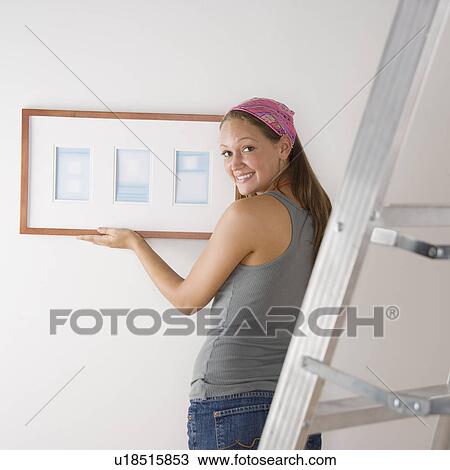 Young woman hanging picture on wall View Large Photo Image Stock Image - Young woman hanging picture on wall. Fotosearch
