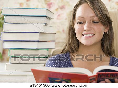 Young woman reading next to stack of books View Large Photo Image Stock Image - Young woman reading next to stack of books. Fotosearch