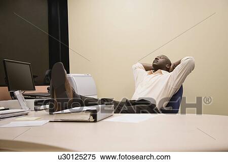 Stock Photography - African businessman relaxing with feet on desk. Fotosearch