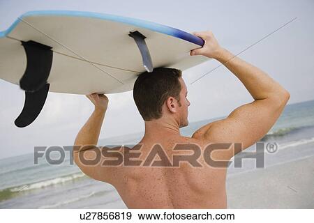 Stock Photo - Bare-chested man holding surfboard. Fotosearch