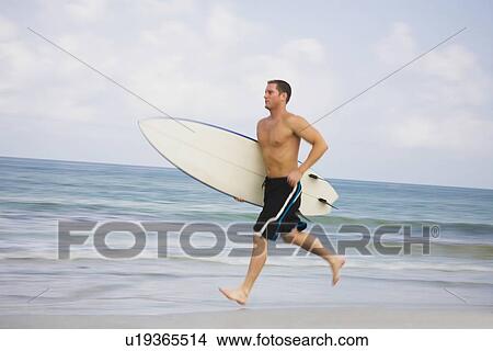 Picture - Bare-chested man running with surfboard. Fotosearch