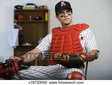 Stock Image - Baseball catcher sitting in locker room looking pensive. Fotosearch
