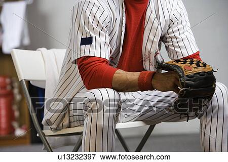 Stock Photo - Baseball player holding glove in locker room. Fotosearch