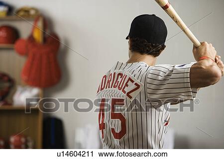 Stock Image - Baseball player practicing swing in locker room. Fotosearch