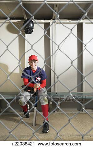 Stock Image - Baseball player sitting in dugout. Fotosearch