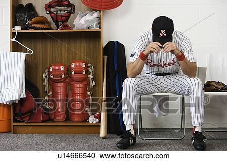 Stock Image - Baseball player sitting with head down in locker room. Fotosearch