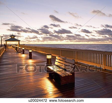 Stock Image - benches on pier during sunrise/sunset. Fotosearch