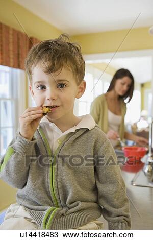 Stock Image - Boy eating cookie on kitchen counter. Fotosearch