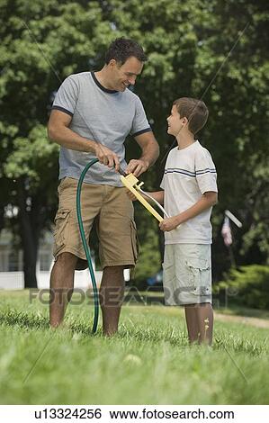 Stock Photograph - Boy helping father with sprinkler in backyard. Fotosearch