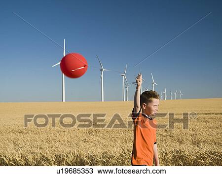 Stock Image - Boy holding balloon on wind farm. Fotosearch