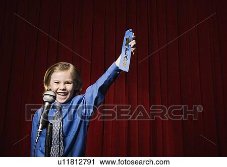 Stock Image - Boy holding first place ribbon on stage. Fotosearch