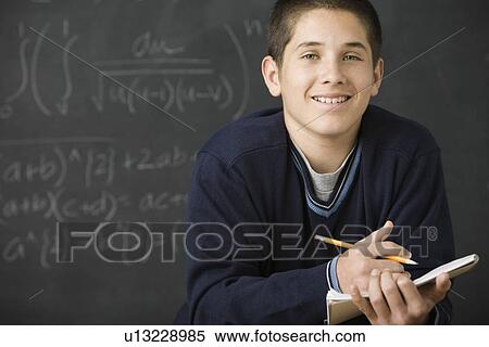 Boy holding notebook in front of blackboard View Large Photo Image Stock Photography - Boy holding notebook in front of blackboard. Fotosearch