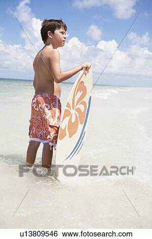 Stock Photograph - Boy holding skimboard in ocean. Fotosearch