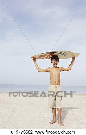 Stock Image - Boy holding skimboard on beach. Fotosearch