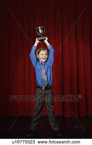 Stock Image - Boy holding trophy on stage. Fotosearch