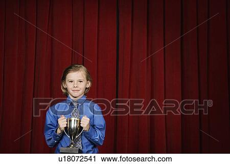 Stock Image - Boy holding trophy on stage. Fotosearch