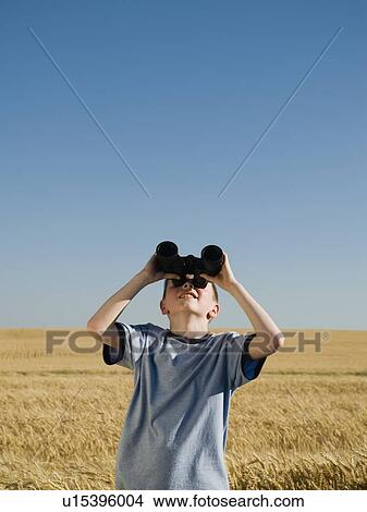Picture - Boy in field looking through binoculars . Fotosearch