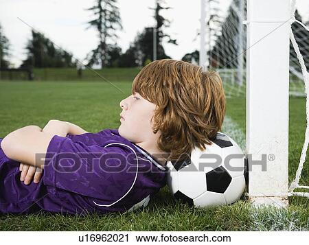 Stock Image - Boy laying on soccer ball against goal. Fotosearch