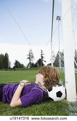 Stock Photograph - Boy laying on soccer ball against goal. Fotosearch