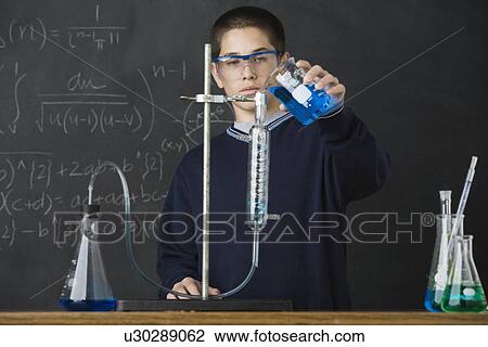 Stock Image - Boy pouring liquid in science class. Fotosearch