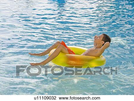 Stock Image - Boy relaxing in inflatable tube in swimming pool. Fotosearch