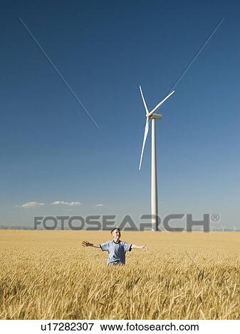 Stock Photo - Boy running through field on wind farm. Fotosearch