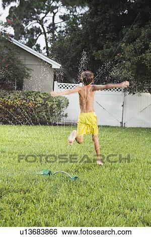 Stock Photograph - Boy running through sprinklers. Fotosearch