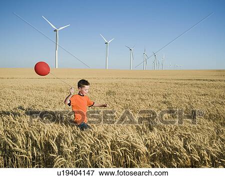 Stock Photo - Boy running with balloon on wind farm. Fotosearch
