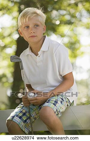 Picture - Boy sitting on fence with golf club and ball. Fotosearch
