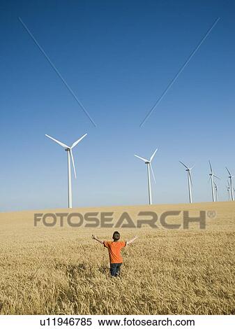 Stock Photography - Boy standing in field on wind farm. Fotosearch