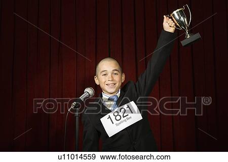 Stock Photo - Boy wearing number and holding trophy. Fotosearch