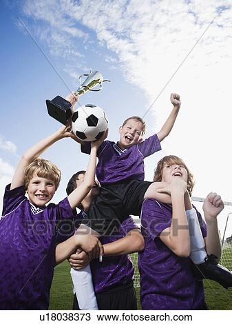 Stock Image - Boys soccer team celebrating with trophy. Fotosearch