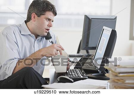 Stock Image - Businessman eating take out food at desk. Fotosearch