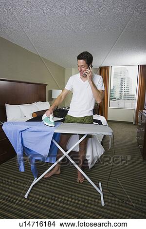 Picture - Businessman ironing shirt and talking on cell phone. Fotosearch