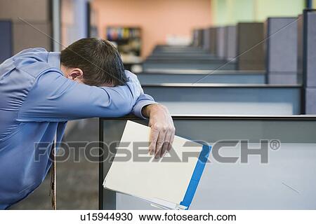 Stock Image - Businessman leaning head on cubicle wall. Fotosearch