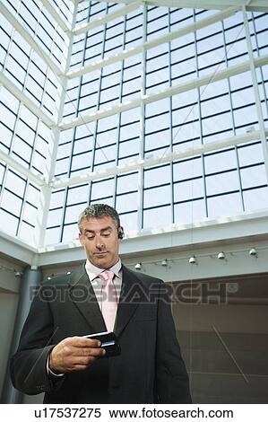 Stock Photography - Businessman looking at cell phone in convention center atrium. Fotosearch
