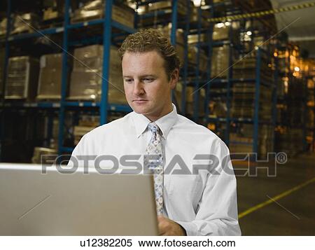 Stock Photography - Businessman looking at laptop in warehouse. Fotosearch