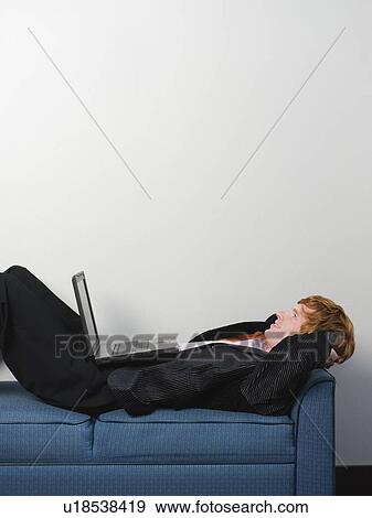Businessman lounging on sofa with laptop View Large Photo Image Stock Photo - Businessman lounging on sofa with laptop. Fotosearch
