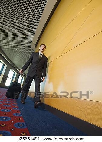 Businessman pulling suitcase in office corridor View Large Photo Image Stock Image - Businessman pulling suitcase in office corridor. Fotosearch